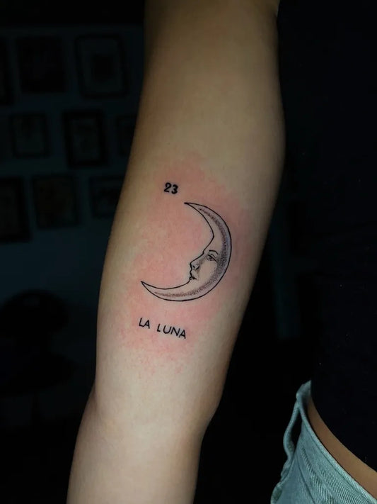 Small Minimalist Crescent Moon with Face and Text Tattoo on Women Arm by @strangelove_tattoo