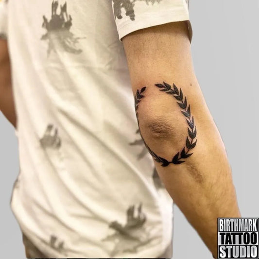 Small Minimalist Laurel Wreath Tattoo on Men Elbow by @birthmarktattoostudio