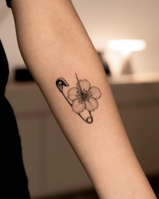 Small Minimalist Safety Pin Holding Cherry Blossom on Women Arm Flower Tattoo by @m_aarte