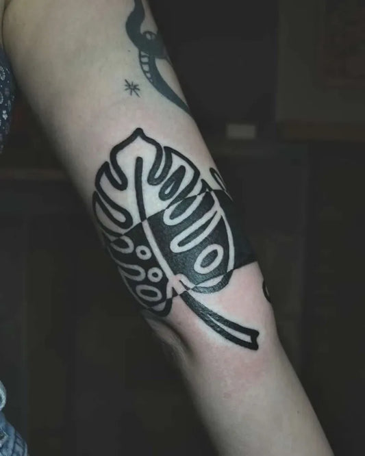 Small Negative Space Monstera Leaf Tattoo on Women Arm by @8ofswordstattoo