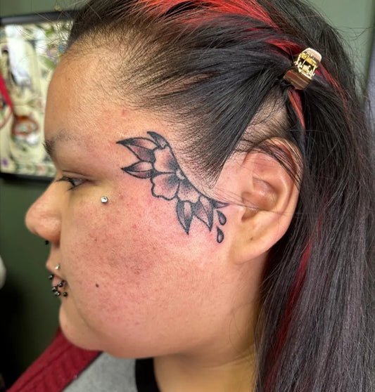 Small Neotraditional Flower and Drips on Women Face Tattoo by @tradbabyy