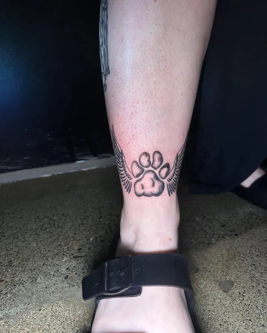 Small Neotraditional Pawprint Wings on Women Ankle Tattoo by @mayberry.ink