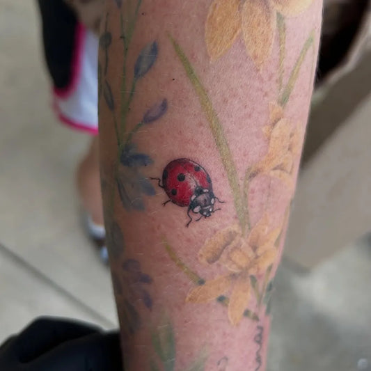 Small Realism Ladybug Daffodils Tattoo on Women Arm by @corinascreations