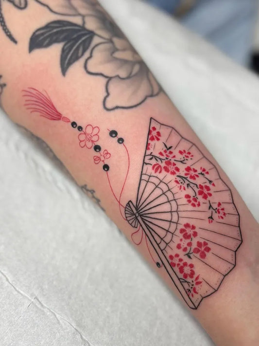 Small Red Fan Tattoo on Women Arm by @lucie.tattoo