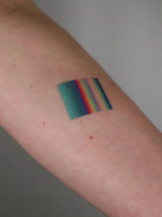 Small Stick and Poke Rainbow Flag Tattoo on Women Arm by @blekanddots