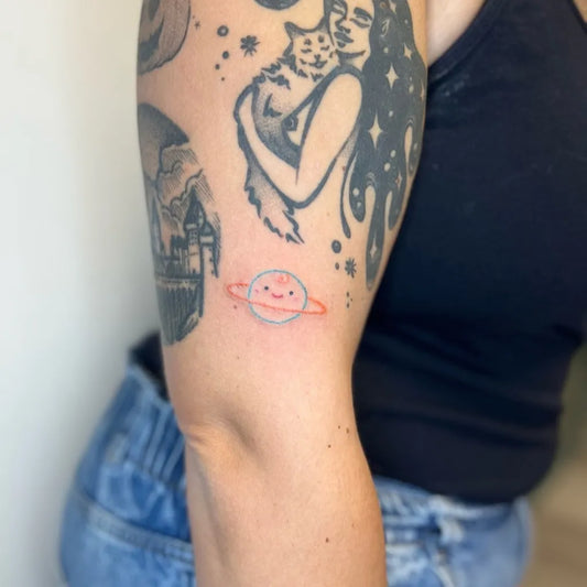 Small Stick and Poke Smiling Saturn Planet Tattoo on Women Arm by @babbygail_doodles