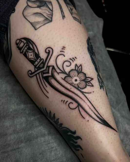 Small Traditional Dagger with Flowers Tattoo on Women Leg by @marissafaithtattoo