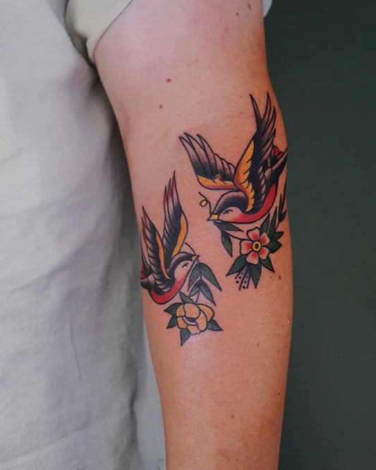 Small Traditional Swallow Flowers Tattoo on Women Arm by @figtree.tattoo.studio