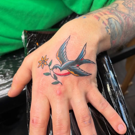 Small Traditional Swallow and Flower Tattoo on Men Hand by @lotte_tattoos
