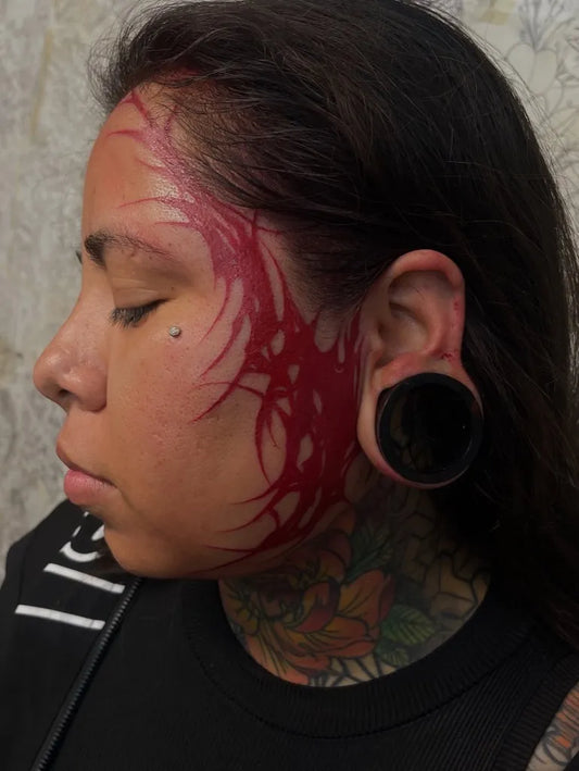 Small Tribal Red Swirls on Women Face Tattoo by @micaela.ink
