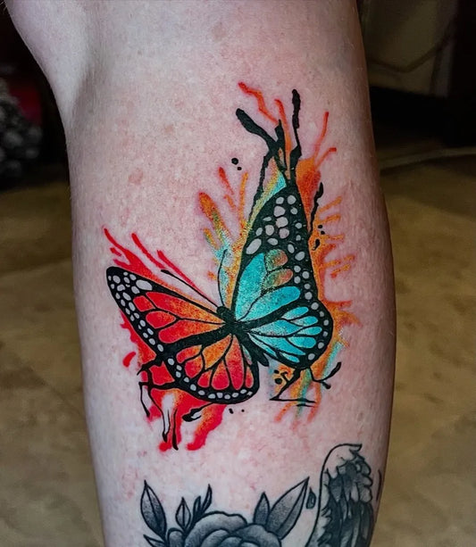 Small Watercolor Butterfly with Splash Effects on Women Leg Tattoo by @miss.mak.ink