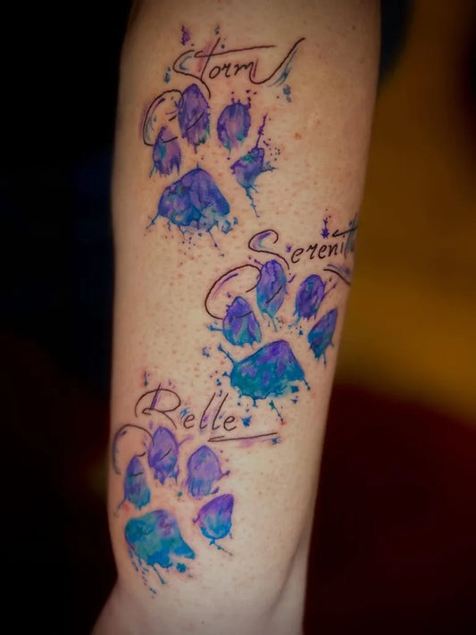 Small Watercolor Paw Prints and Names on Women Arm Tattoo by @elyse.ink