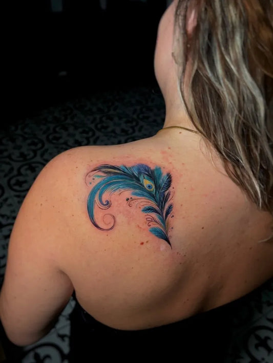 Small Watercolor Peacock Feather Tattoo on Women Shoulder by @betatattoo.studio