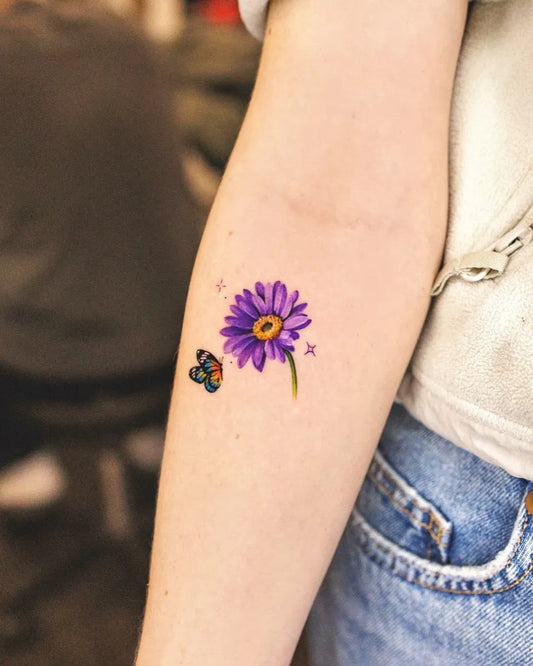 Small Watercolor Purple Gerbera Daisy and Butterfly Tattoo on Women Arm by @ssuncolor