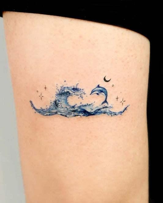 Small Watercolor Wave Dolphin Moon Tattoo on Women Thigh by @suryeon.tattoo