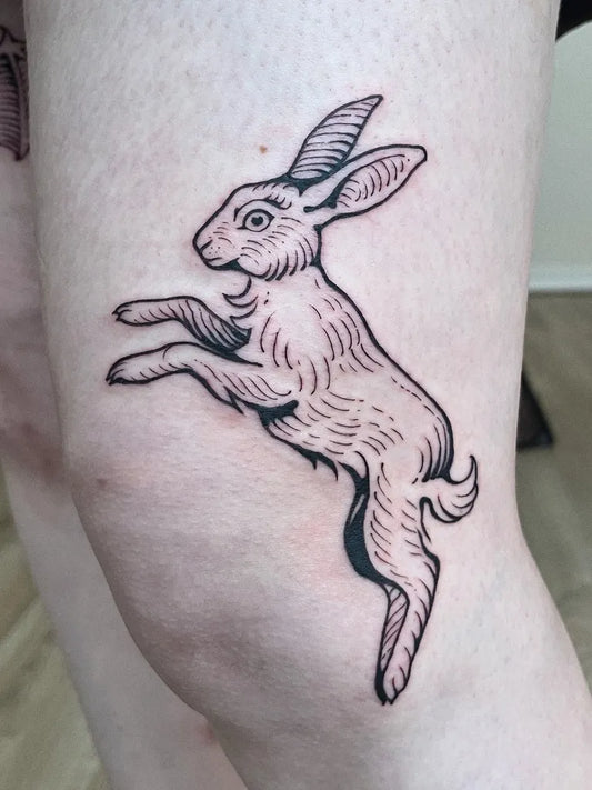Small Woodcut Jumping Rabbit Tattoo on Women Thigh by @j.laakkonentattoo