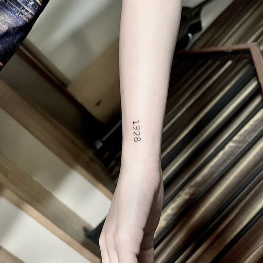 Tiny Black and Grey Numerals 1928 Tattoo on Women Wrist by @fatcowtattoo