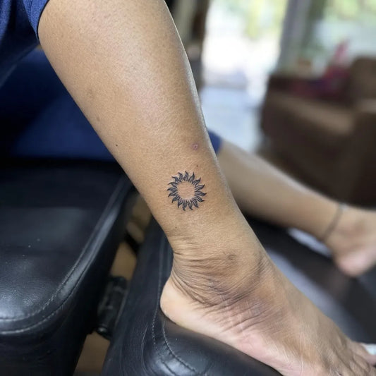 Tiny Black and Grey Sun on Women Ankle Tattoo by @feather_art_studio_