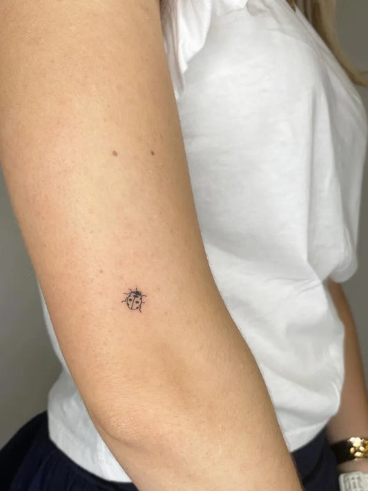 Tiny Blackwork Ladybug Tattoo on Women Arm by @goodluck.tattoomallorca