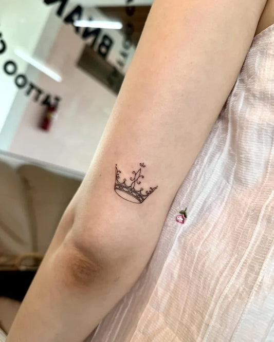 Tiny Fine Line Crown Tattoo on Women Arm by @bnanatattoo