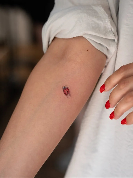 Tiny Fine Line Ladybug Tattoo on Women Arm by @fat_cat.tattoo