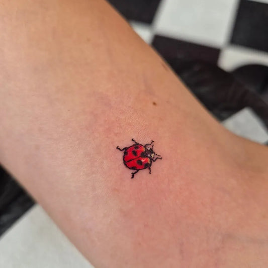 Tiny Fine Line Ladybug Tattoo on Women Arm by @joyofinktattoos
