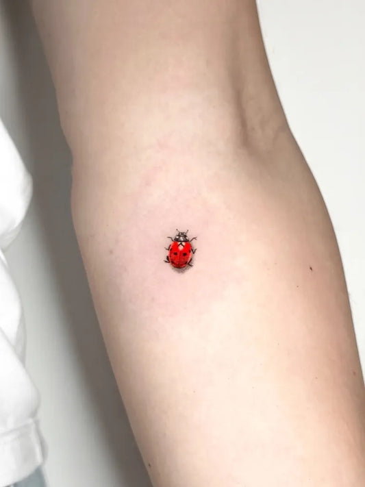 Tiny Fine Line Ladybug Tattoo on Women Arm by @tattoobycoco