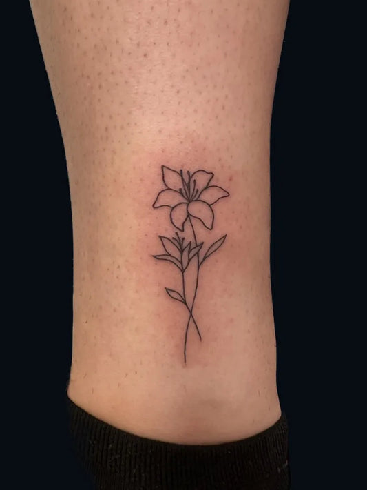 Tiny Fine Line Lily Flower with Leaves on Women Leg Tattoo by @blackcaveotrtattoo