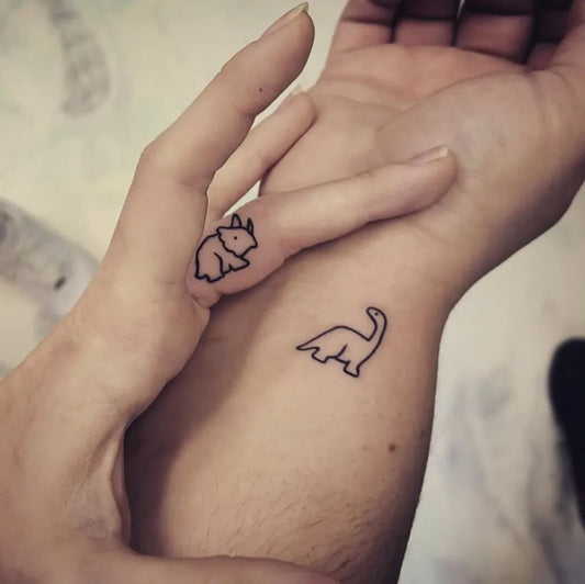 Tiny Linework Bunny and Brachiosaurus on Women Wrist Tattoo by @bluebirdtattoostudio