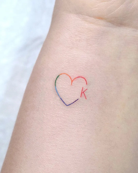 Tiny Linework Rainbow Heart with K on Women Wrist Tattoo by @ziv_tattooer