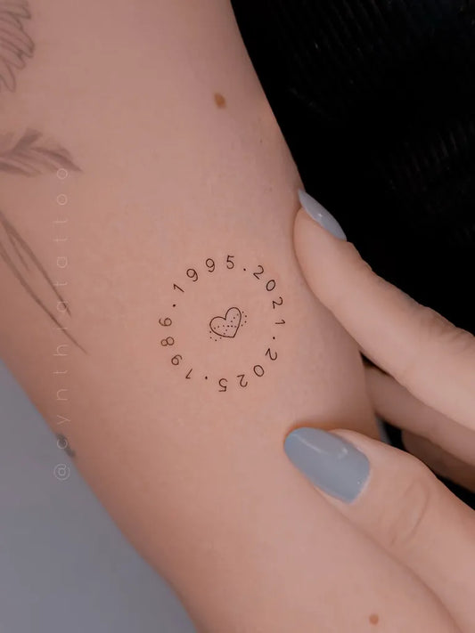 Tiny Minimalist Circular Dates with Heart on Women Arm Tattoo by @cynthiatattoo