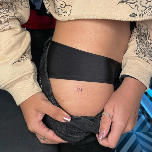 Tiny Minimalist Number Tattoo on Women Hip by @mike.tats
