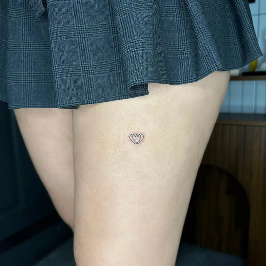 Tiny Minimalist Outline Heart on Women Thigh Tattoo by @_tan_tattoo