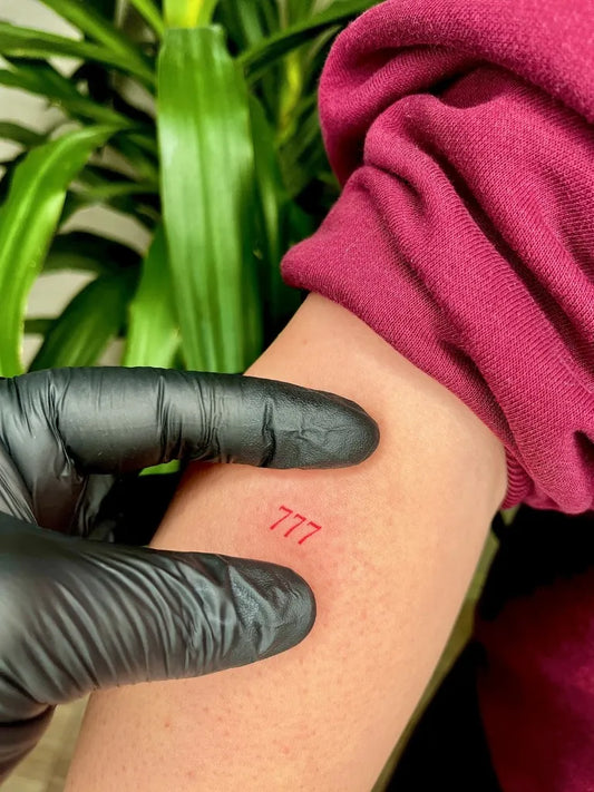 Tiny Minimalist Red 777 Tattoo on Women Forearm by @inkora.tattooo