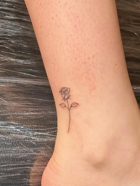 Tiny Minimalist Rose with Stem and Leaves on Women Ankle Tattoo by @tatts.by.pat