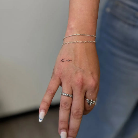 Tiny Minimalist XO text on Women Hand Tattoo by @skinandbrows.ink