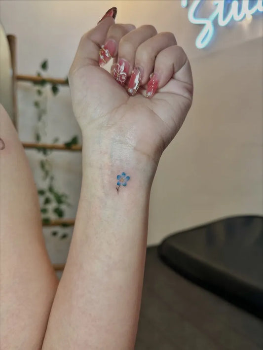Tiny Minimalist blue flower on Women wrist Tattoo by @des.piercinkstudio