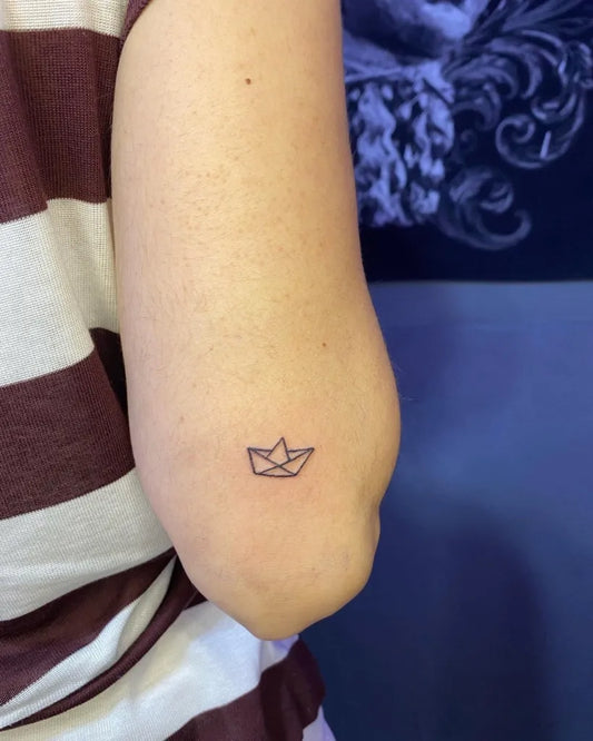 Tiny Minimalist origami boat on Women upper arm Tattoo by @bocek.ink