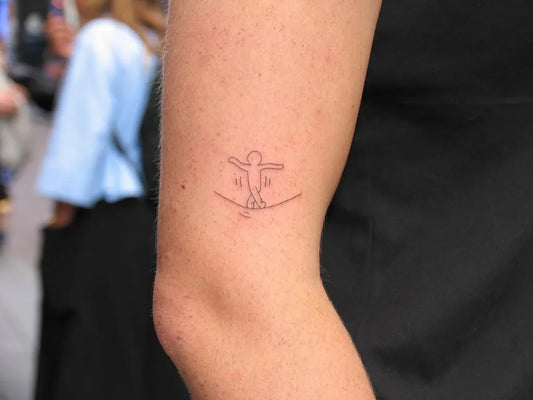 Tiny Minimalist stick figure balancing on tightrope on Women upper arm Tattoo by @inkigai.studio