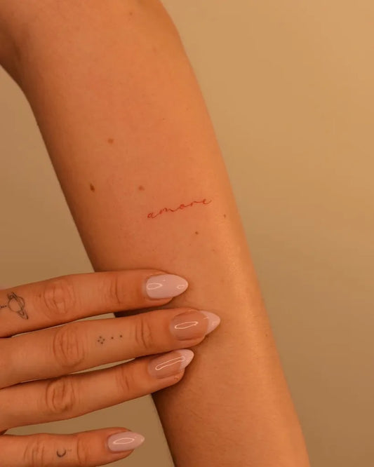 Tiny Red Word Tattoo on Women Arm by @gwen.tattooing