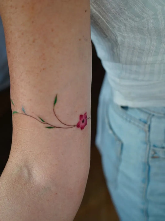 Tiny Watercolor Stem with Leaves and Flower on Women Arm Tattoo by @barisyesilbas