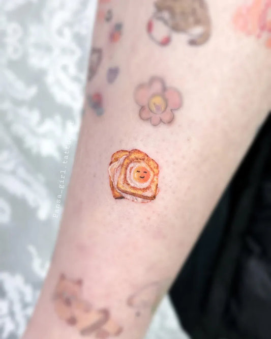 Tiny Watercolor Toast and Flowers on Women Arm Tattoo by @pansa_girl.tattooist