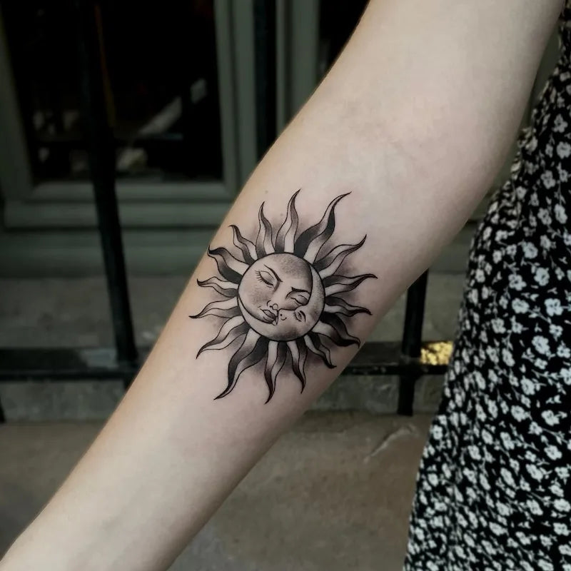 black and grey tribal sun tattoo on inner forearm