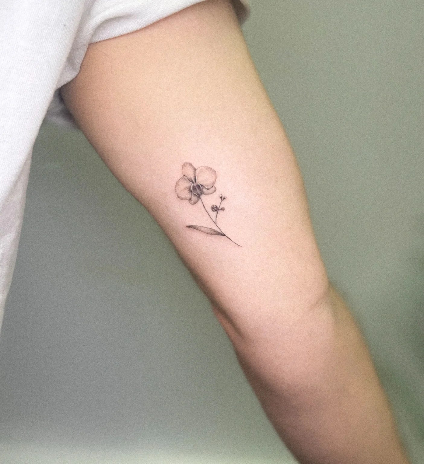 small micro realism single needle black and grey flower tattoo on woman bicep
