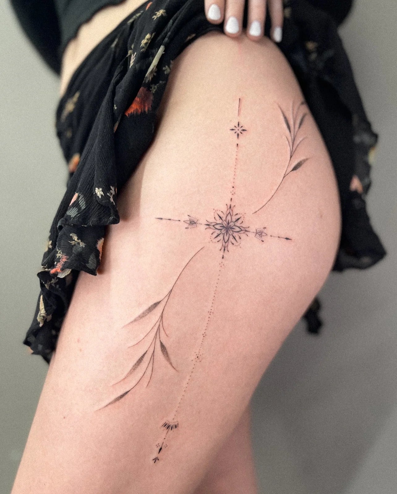 single needle tattoo of a snowflake design on woman hip with a floral-patterned top