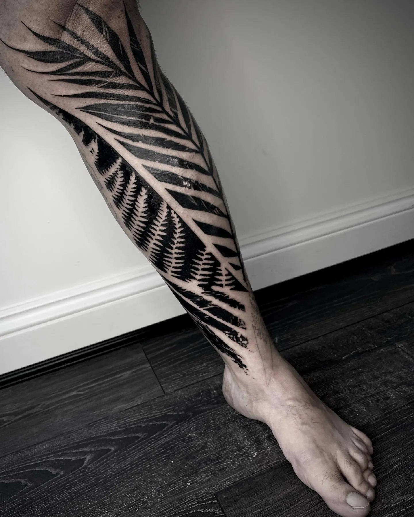 blackwork tattoo leaf pattern on man leg