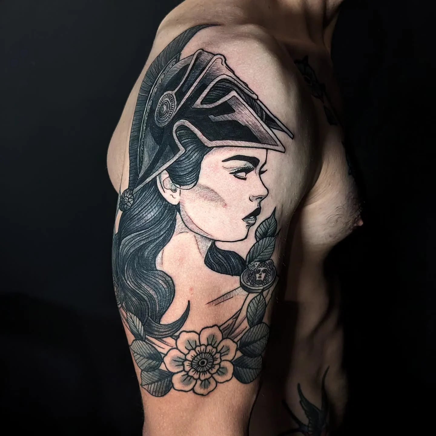 Tattoo of a woman's face with a helmet and floral design on man upper arm
