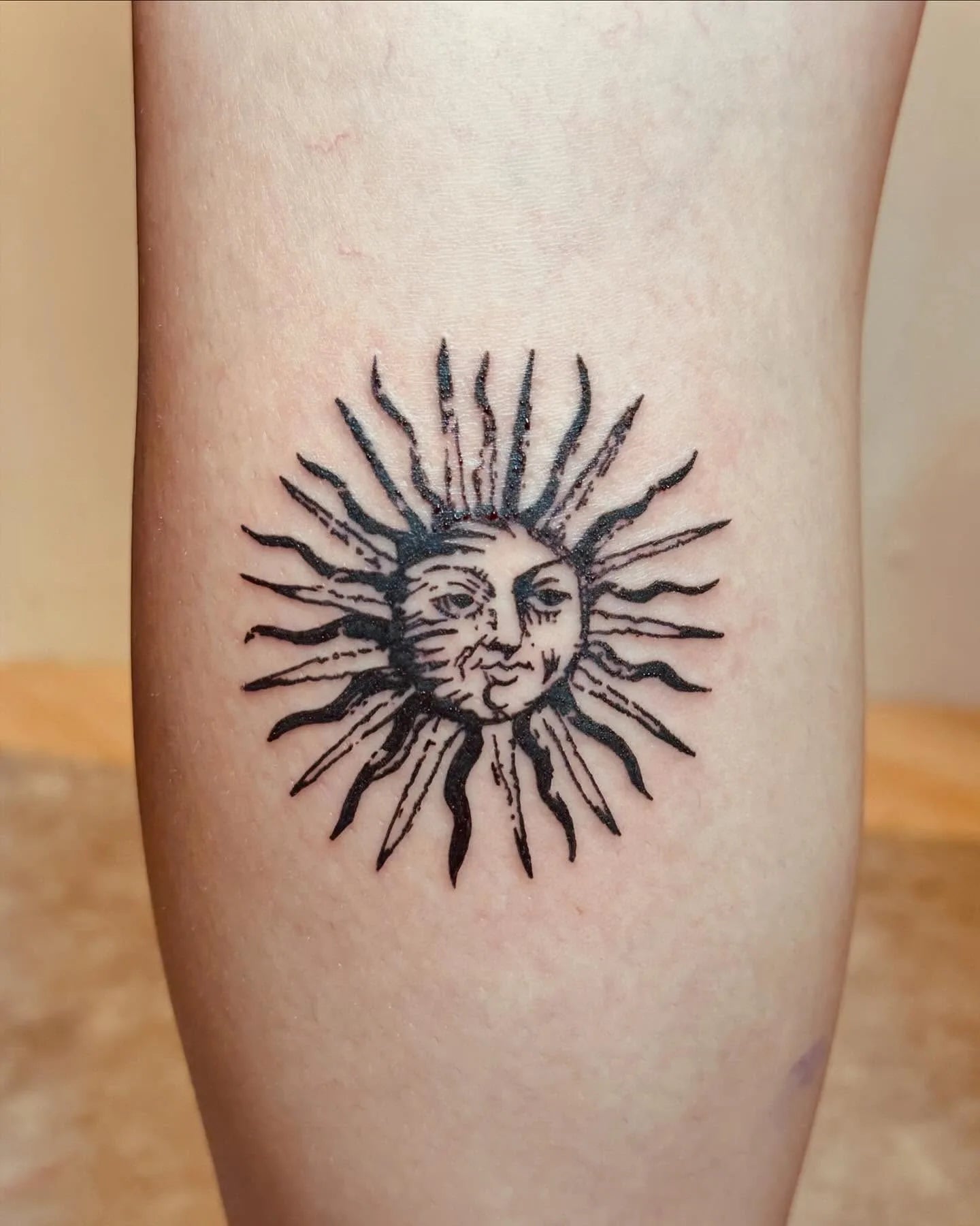tribal sun with face tattoo on calf leg