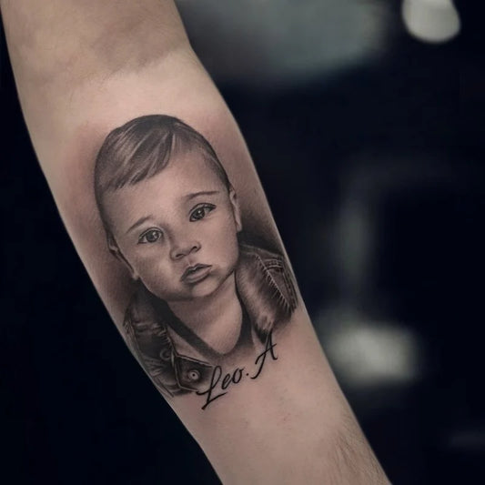 baby child face portrait memorial black and grey realism tattoo on forearm