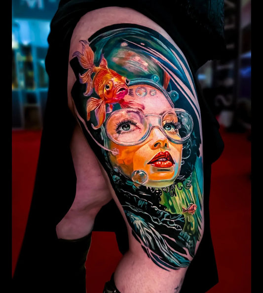 Colorful tattoo of a woman with fish and bubbles on a person's arm.